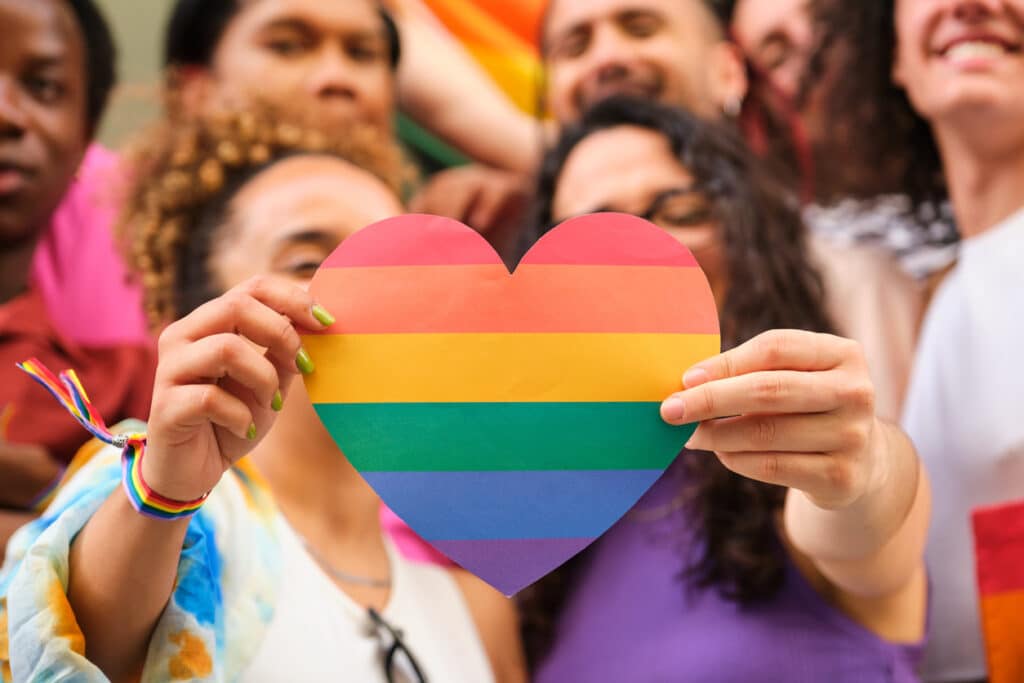 a group of lgbtq people holding a rainbow heart celebrating pride month.