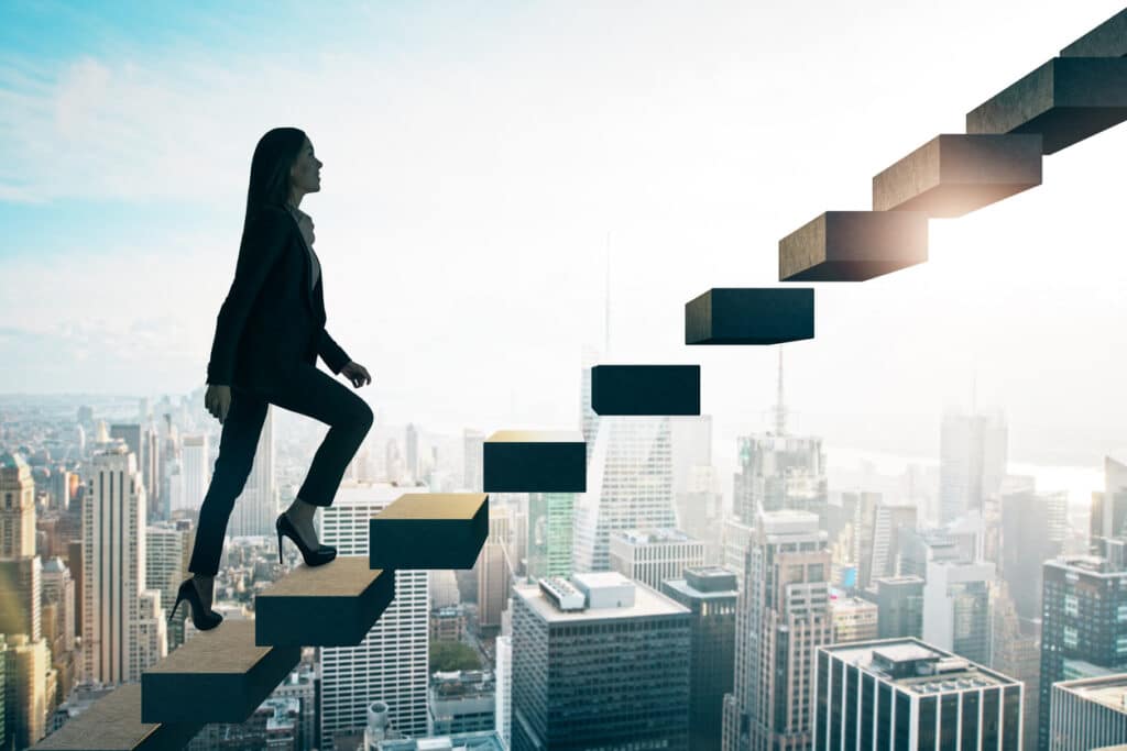 road to success concept with businesswoman going up the stairs on sunny megapolis city background.